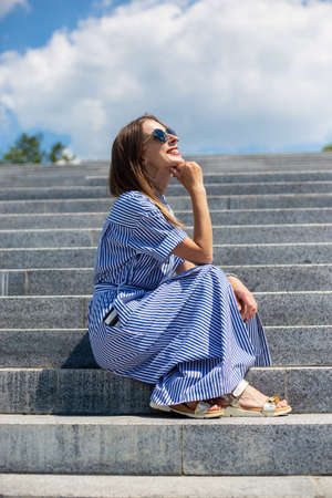 Young woman in dress sits on steps in the park.