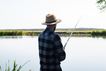 Man in a hat and a plaid shirt is fishing on a line by the river.の写真素材