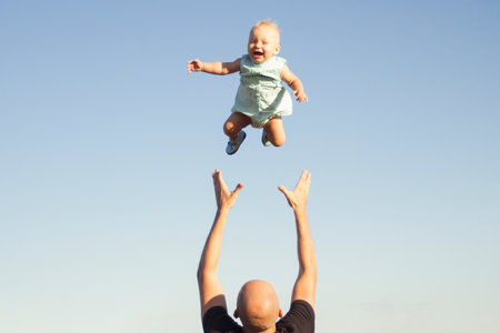 Dad throws his child up against the blue sky. Concept game with children, happy family.の写真素材