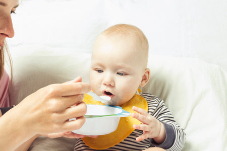 Young mother feeds a small child with a spoon. Concept of starting feeding baby solid food.