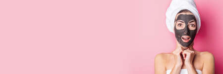 surprised young woman with closed eyes with black mask on her face on a pink background. Banner