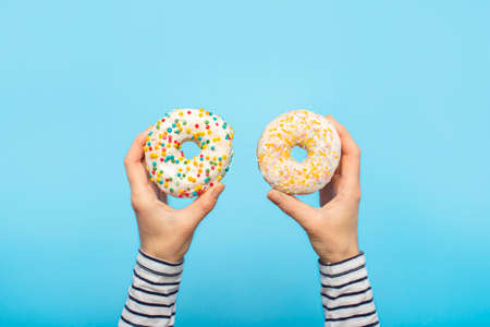 Female hands hold donuts on a blue background. Concept confectionery store, pastries, coffee shop. Banner. Flat lay, top view.の写真素材