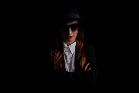 beautiful business elegant woman in a hat, glasses in the dark on a black background.の写真素材