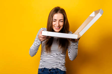 cheerful young woman enjoying the aroma of fresh hot pizza on yellow background.