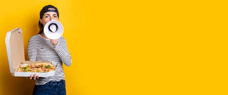 smiling young woman pizza delivery man shouting into a megaphone while holding pizza on yellow background. Banner.の写真素材