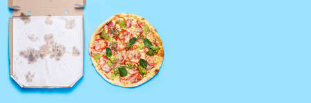 pizza and empty open pizza packaging on blue background. Top view, flat lay. Banner.の写真素材