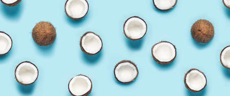 many open coconut halves and a leaf of a palm tree on a blue background. Top view, flat lay. Banner.