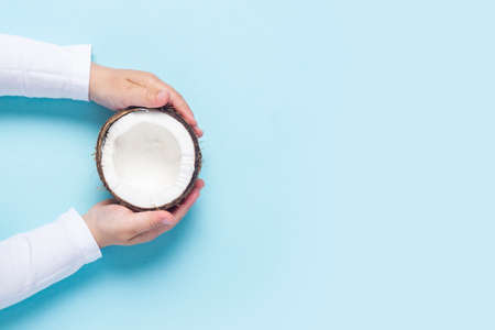 children's hands are holding half a coconut on a blue background. Top view, flat lay.