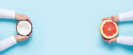 children's hands hold half a grapefruit and half an orange on a blue background. Top view, flat lay....