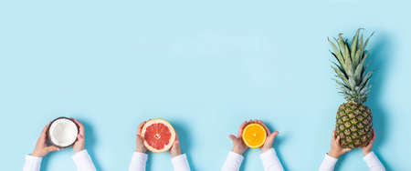 childrens hands hold coconut, grapefoot, orange and whole pineapple on a blue background. Top view, flat lay. Banner.の写真素材