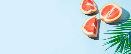 cut halves of a grapefruit and a leaf of a palm tree on a blue background. Top view, flat lay. Banner.の写真素材