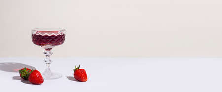 glass with red wine and strawberries on the table on a light background. Banner.の写真素材