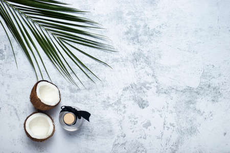 Opened coconut, bottle and palm leaf on concrete background. Top view, flat lay.