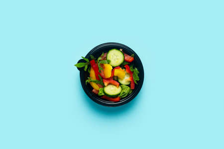 Vegetable salad in a plastic disposable bowl on a light blue background. Top view, flat lay.