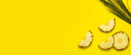 Ripe pineapple slices, pineapple with foliage and a palm leaf on a yellow background. Top view, flat lay.の写真素材