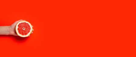 A female hand holds half a grapefruit on a red background. Top view, flat lay.