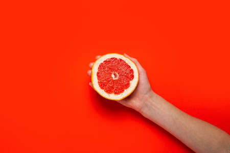 A female hand holds half a grapefruit on a red background. Top view, flat lay. Banner.の写真素材