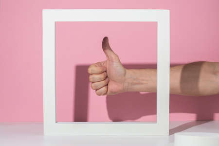 Male hand showing thumb up in white square podium for presentation on pink background.の写真素材