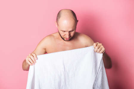 Young nude man holding a white towel on a pink background.の写真素材