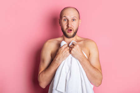Surprised young nude man covered with towel over pink background.の写真素材