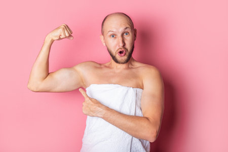 Surprised young man shows finger to biceps on pink background.の写真素材