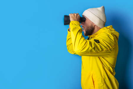 young man in a yellow jacket looks through binoculars on a blue background.の写真素材