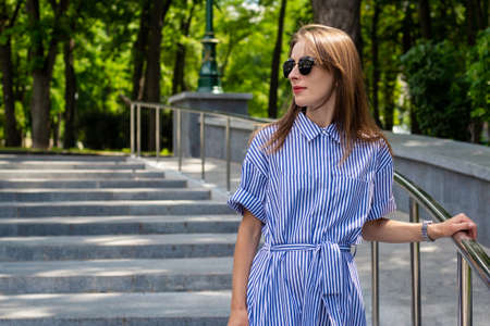 Young woman in dress and glasses descends the stairs in the park.
