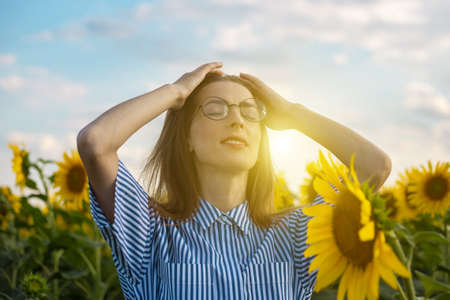 Young woman in dress and glasses at sunset on a sunflower field.の写真素材