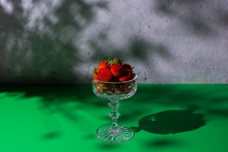 Fresh strawberries in a glass under natural light on a concrete and green table background.の写真素材