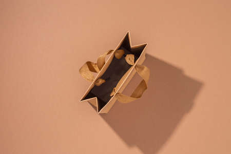 Craft gift packet with satin ribbon on brown background. Top view, flat lay.