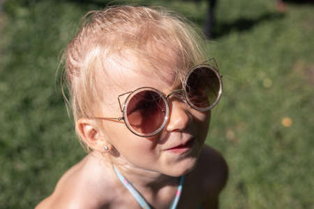 Smiling little girl in a swimsuit in sunglasses in a city park.