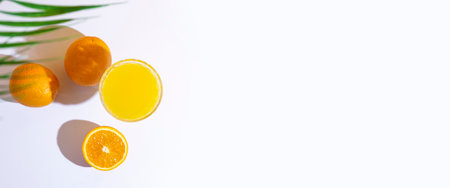 glass with fresh juice, oranges and a leaf of a palm tree on a light background. Top view, flat lay....