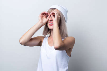 Cheerful young woman making binoculars shape with fingers on light background.の写真素材