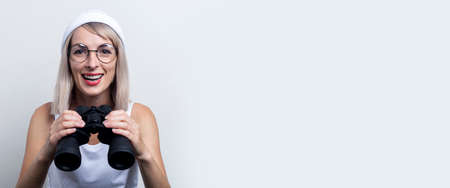 Smiling young blonde woman with binoculars on a light background. Banner.の写真素材