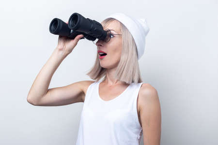 Surprised young woman looking through binoculars on a light background.の写真素材