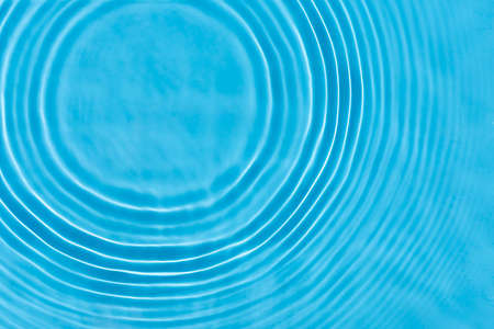 Wave from a drop of water on blue water under natural light. Top view, flat lay.の写真素材