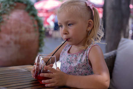 Child drinks a drink on the summer terrace under natural light. Real people.の写真素材