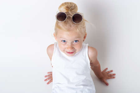 Smiling child in sunglasses posing on a light background in the studio.