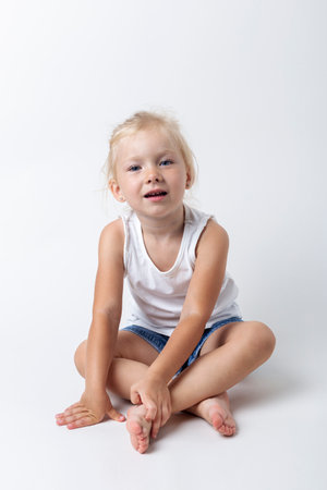 Child in a T-shirt, shorts sitting in the studio on a light background.の写真素材
