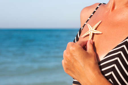 Woman on the beach in a swimsuit holding a starfish on the chest.の写真素材