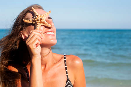 Smiling young woman with starfish closes her eye with starfish on the background of the sea.の写真素材