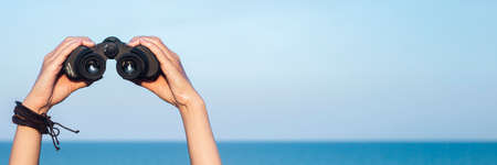 Female hands hold binoculars against the background of the sky and the sea. Banner.の写真素材