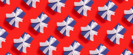 Lots of Christmas gift boxes blue with a white ribbon on a red background. Top view, flat lay. Banner.の写真素材