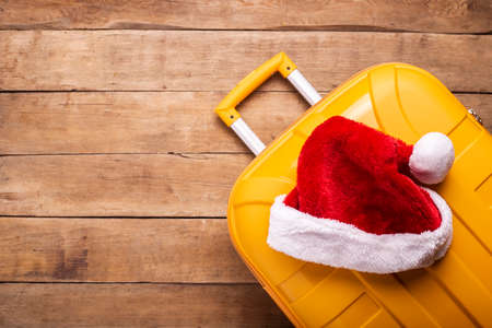 Santa claus hat lies on a yellow suitcase on a wooden background. Top view, flat lay.の写真素材