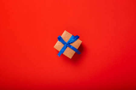 Gift wrapped in craft paper with blue ribbon on red background. Top view, flat lay.の写真素材