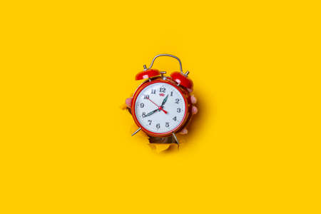 Hand holds a red watch in a hole in a torn yellow background.