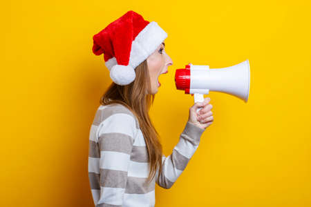 Young woman shouts into a megaphone on a yellow background.の写真素材