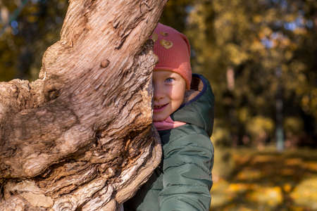Smiling child girl hiding behind a tree in the parkの写真素材