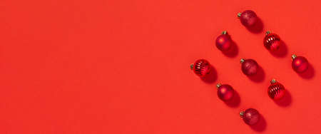 Beautiful red small decorative balls are scattered on a red background. Top view, flat lay. Banner