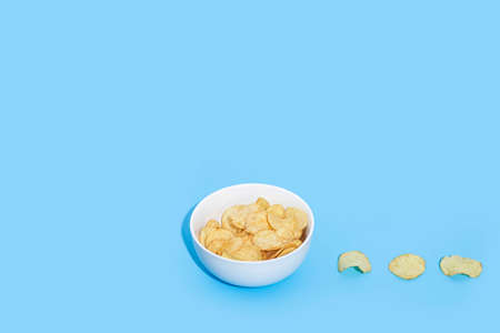 Potato chips in a white bowl on a blue background. Top view, flat layの写真素材